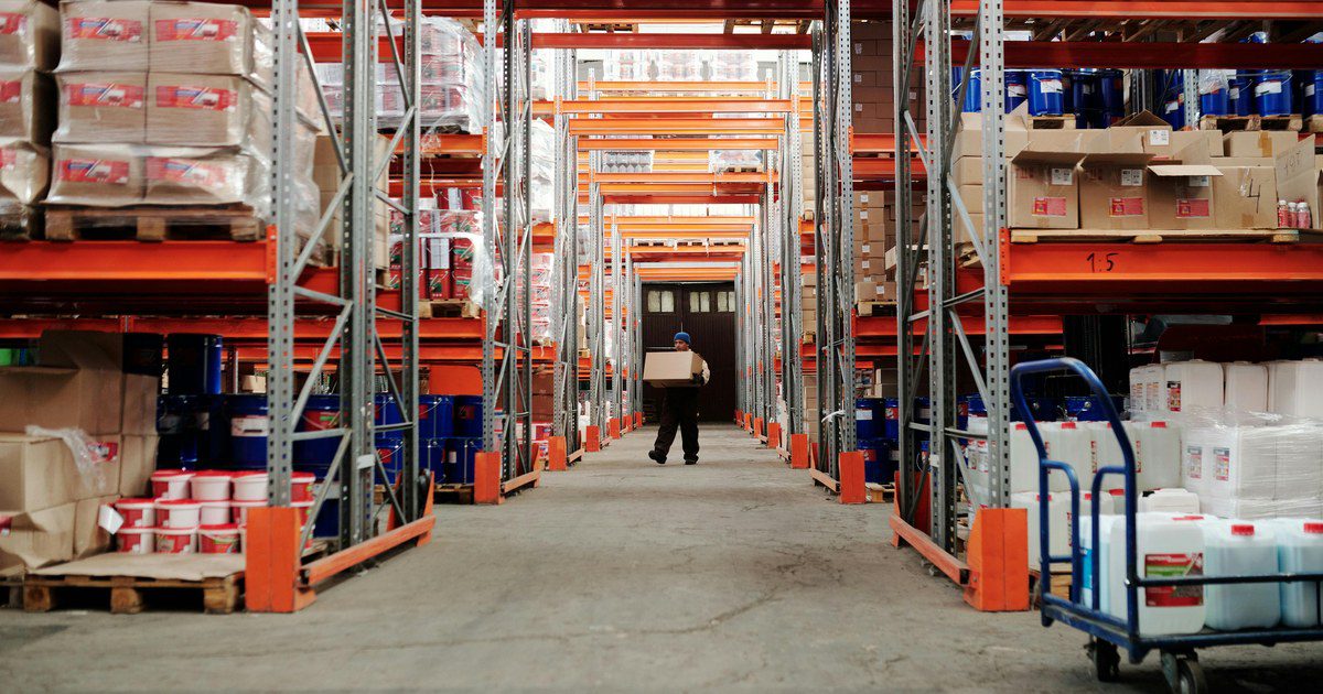 A worker carrying a box in a well-organized warehouse storage aisle.