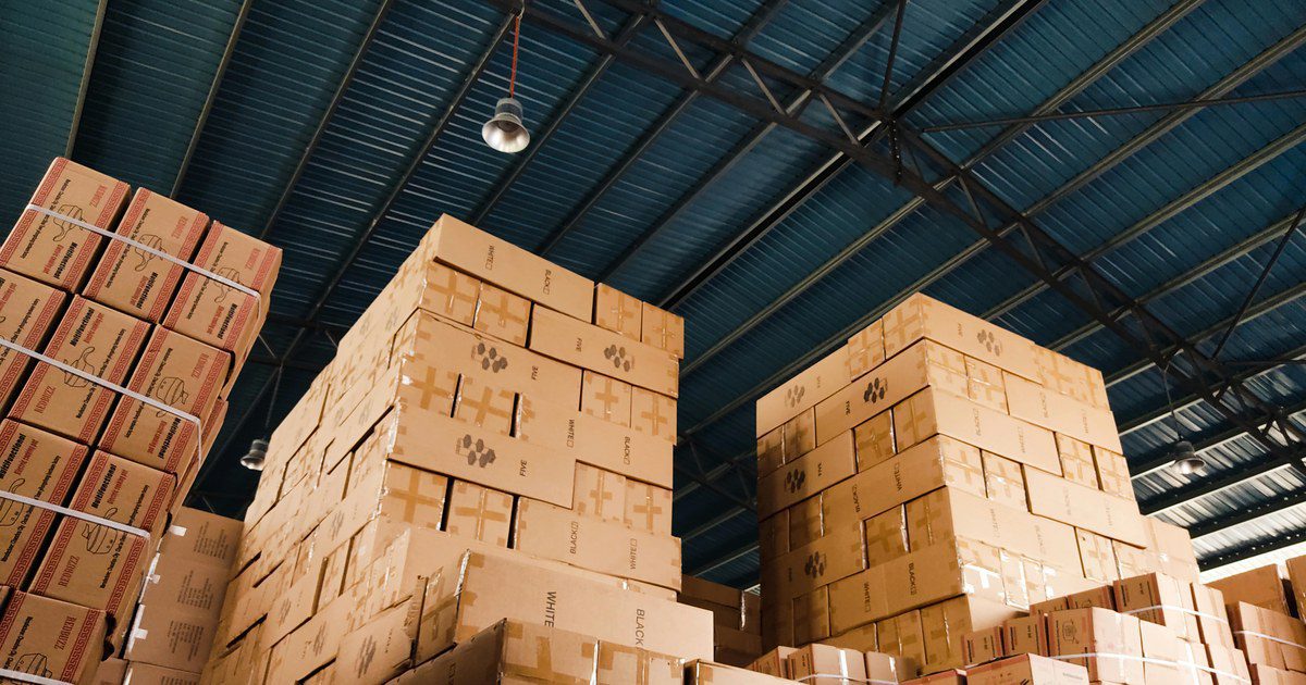 High stacks of cardboard boxes organized in a warehouse with a blue metal ceiling.