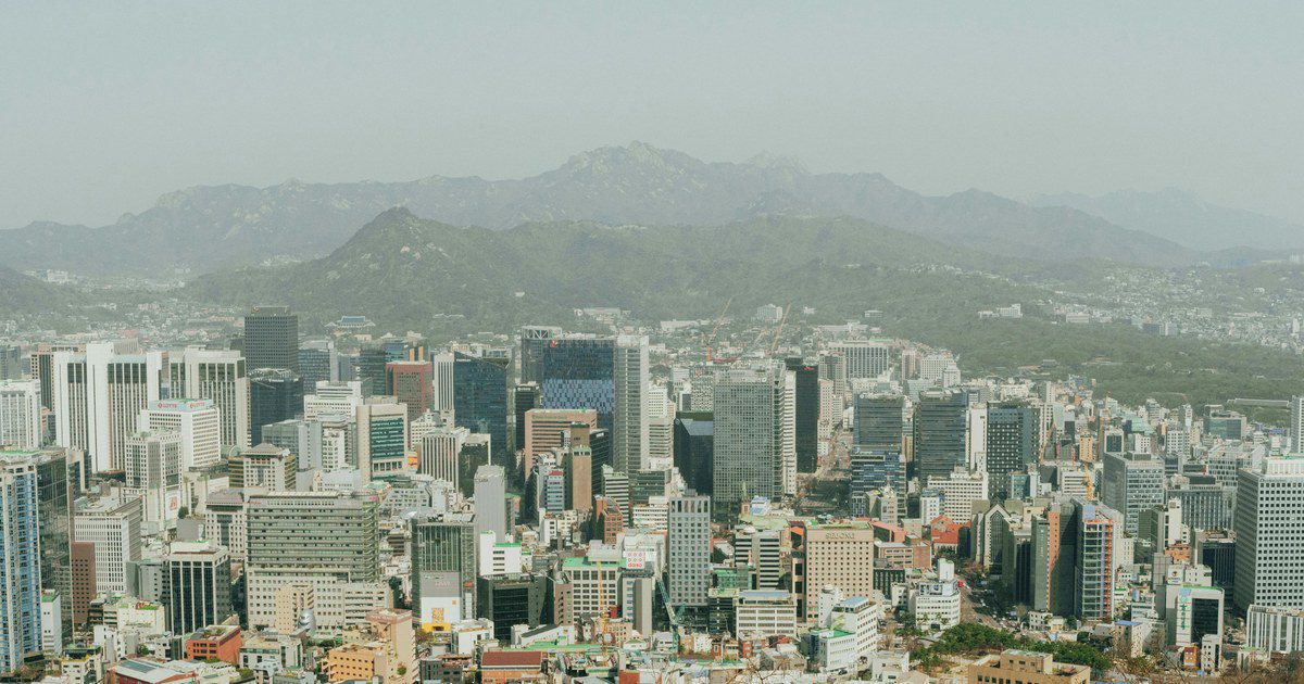 Panoramic aerial view of Seoul's skyscrapers with surrounding mountains, depicting modern urban landscape.