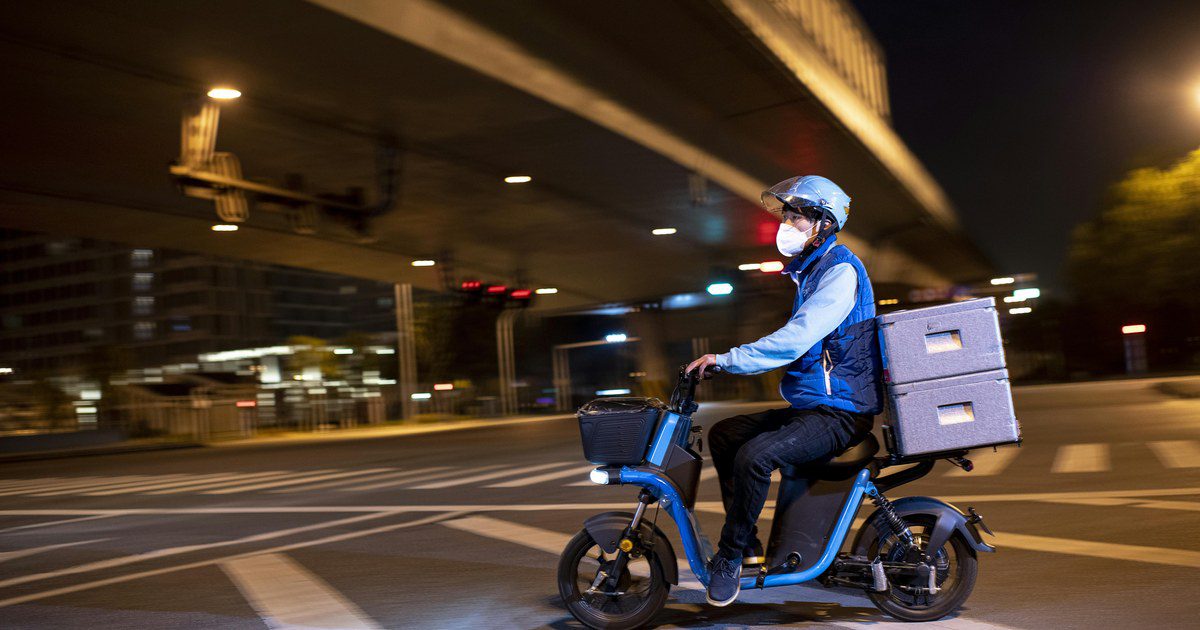 A masked delivery driver rides an electric scooter on Wuhan city streets at night.