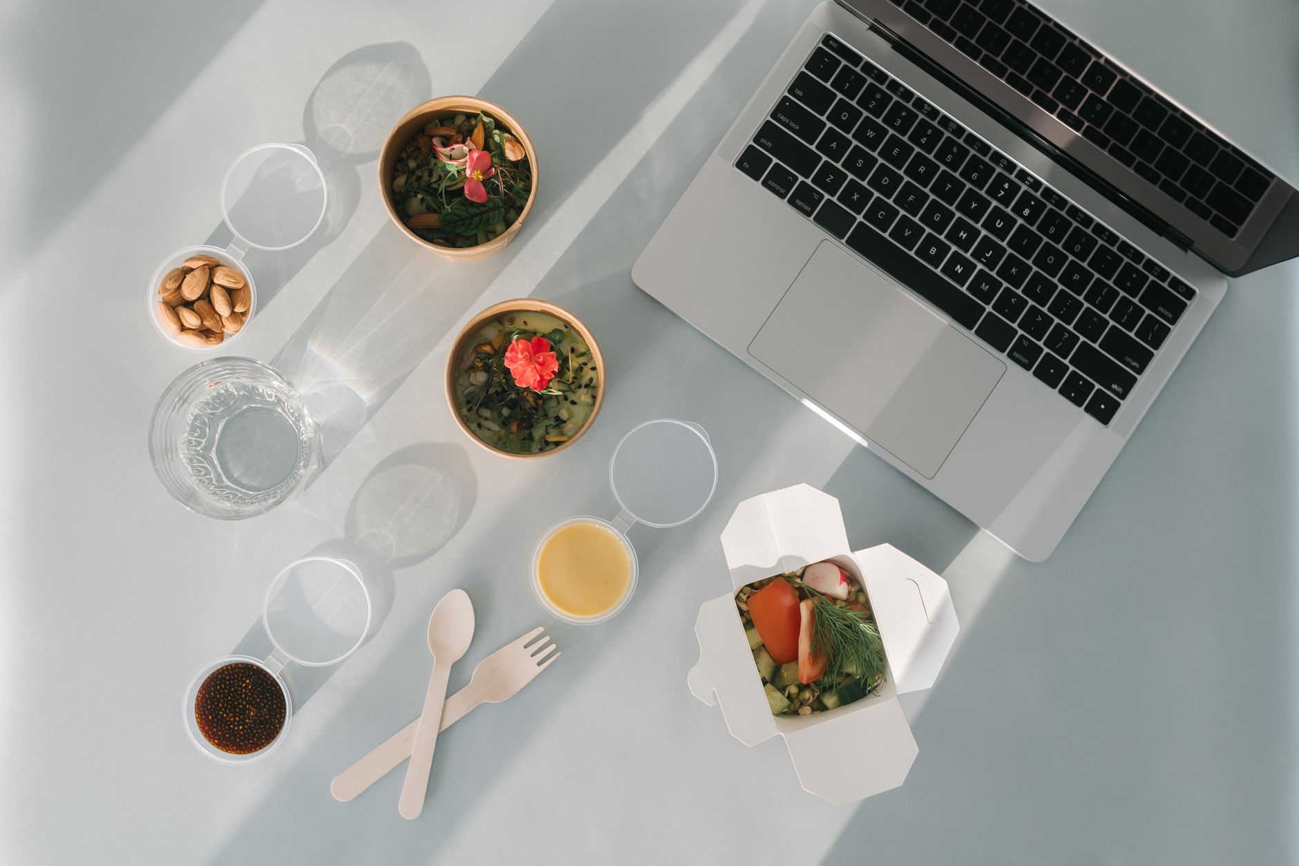 a laptop beside bowls of healthy foods on a white surface